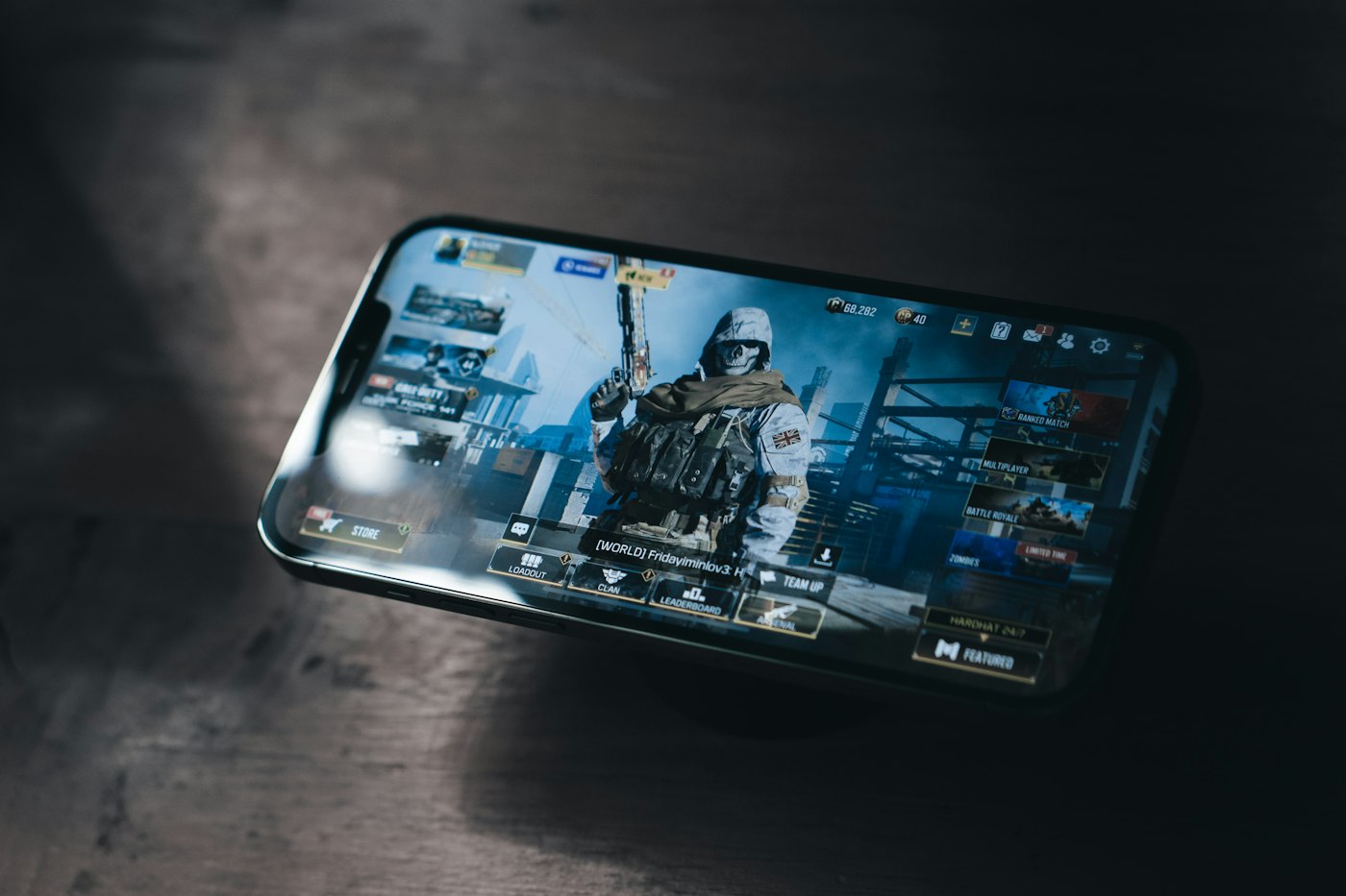 Smartphone menampilkan game battle royale di atas meja kayu